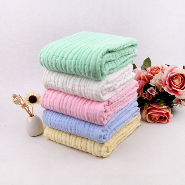 Neatly folded stack of cotton muslin baby blankets with a mint blanket on top